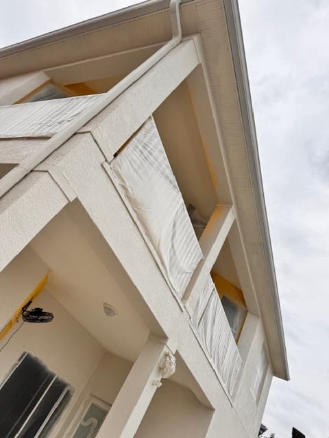 Exterior painting prep on a two-story stucco home with masked windows, trim, and entry details