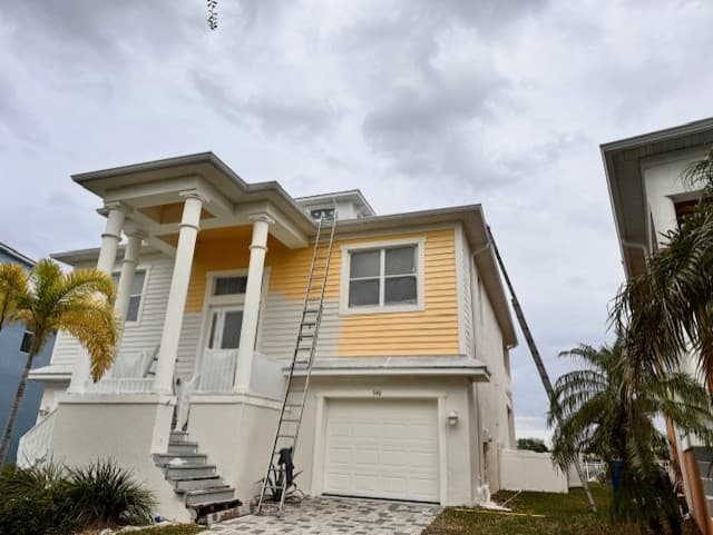 Before photo of a two-story exterior repaint showing original yellow siding and active prep work