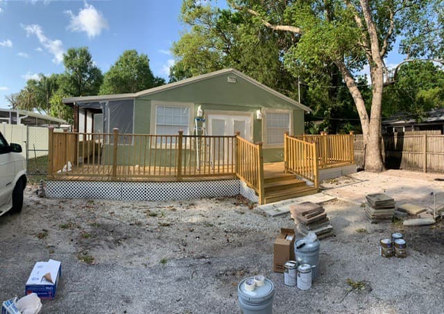 Before photo of a small home exterior with green siding and natural wood deck rails before repainting