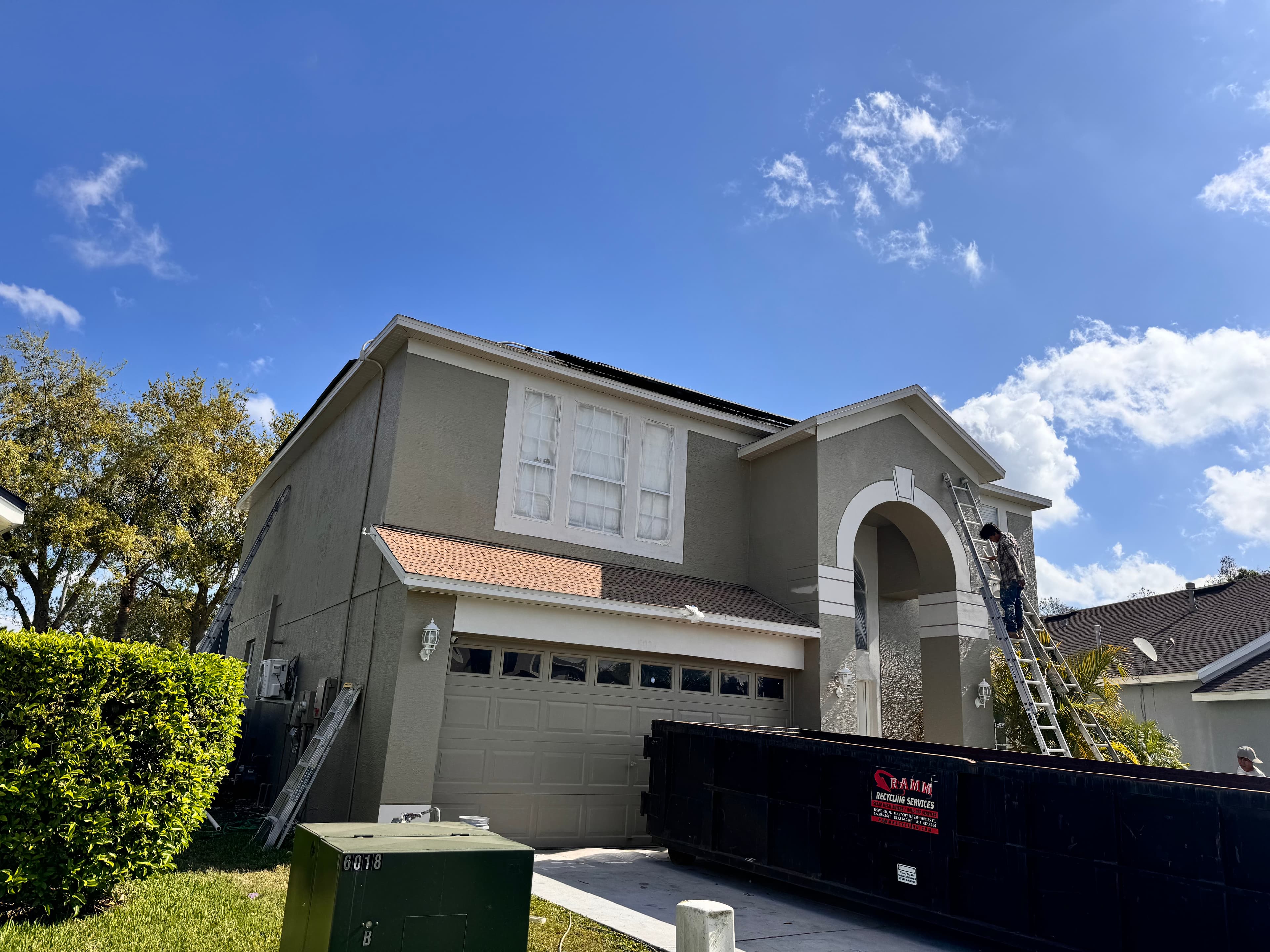 Exterior repaint in progress on a two-story stucco home with ladders, masking, and active prep work